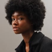 Portrait of Jessica Randall with natural curly hair, wearing a black outfit, and looking directly at the camera.